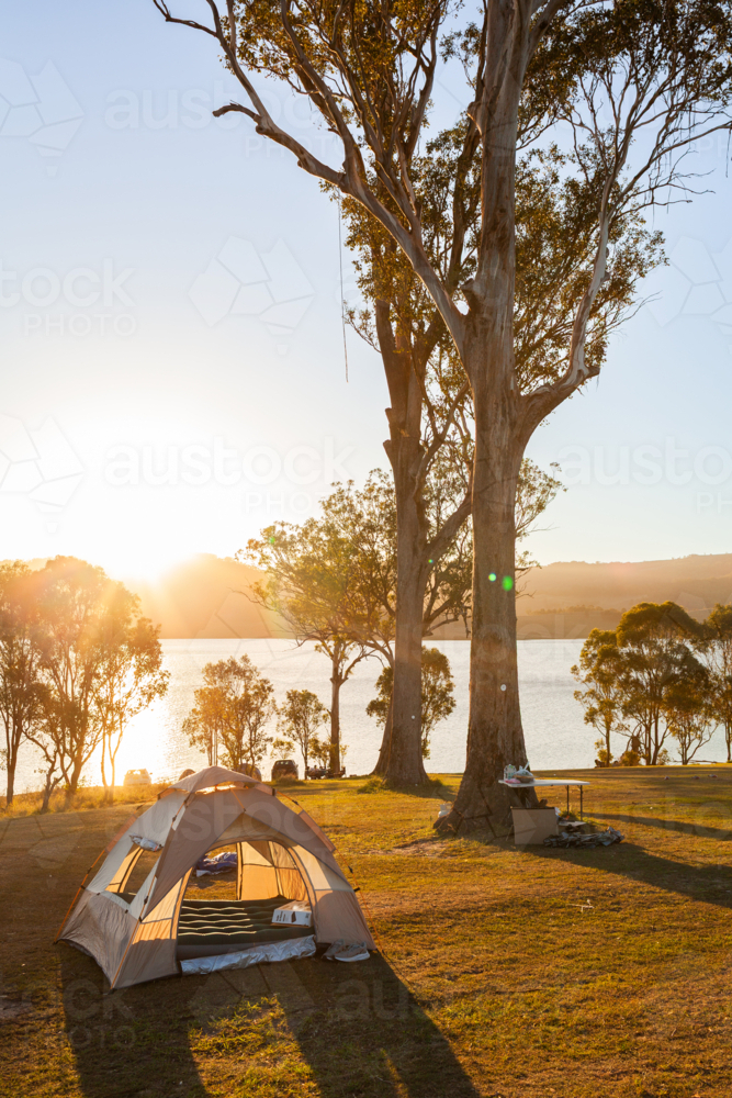Tent pitched on hilltop in campground beside lake in golden Australian sunlight - Australian Stock Image