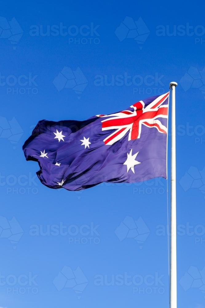 The Australian Flag waving proudly under a clear blue sky - Australian Stock Image