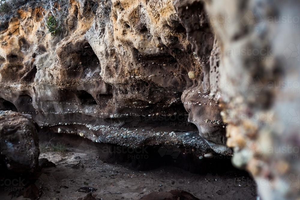 The entrance of a small, dark sandstone cave covered in a variety of tiny naturally embedded pebbles - Australian Stock Image