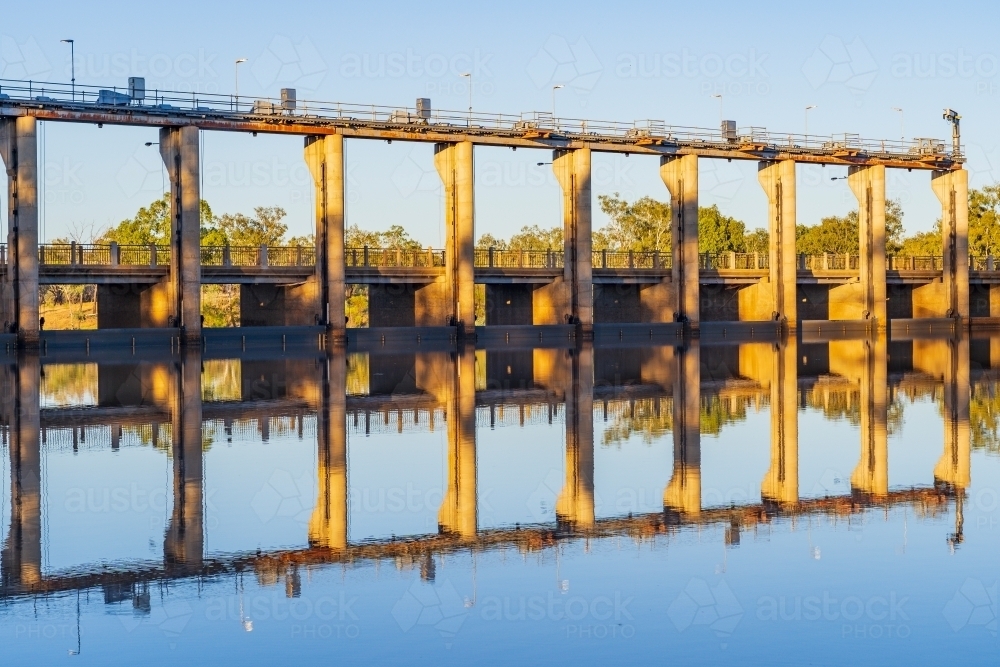 The flood gates of a tall weir reflected in the water of a calm river - Australian Stock Image