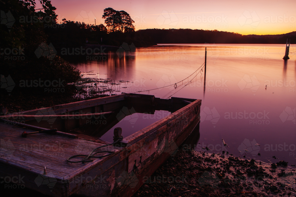 The idyllic setting across Wagonga Inlet and a disused boat at sunset in Narooma, NSW, Australia - Australian Stock Image