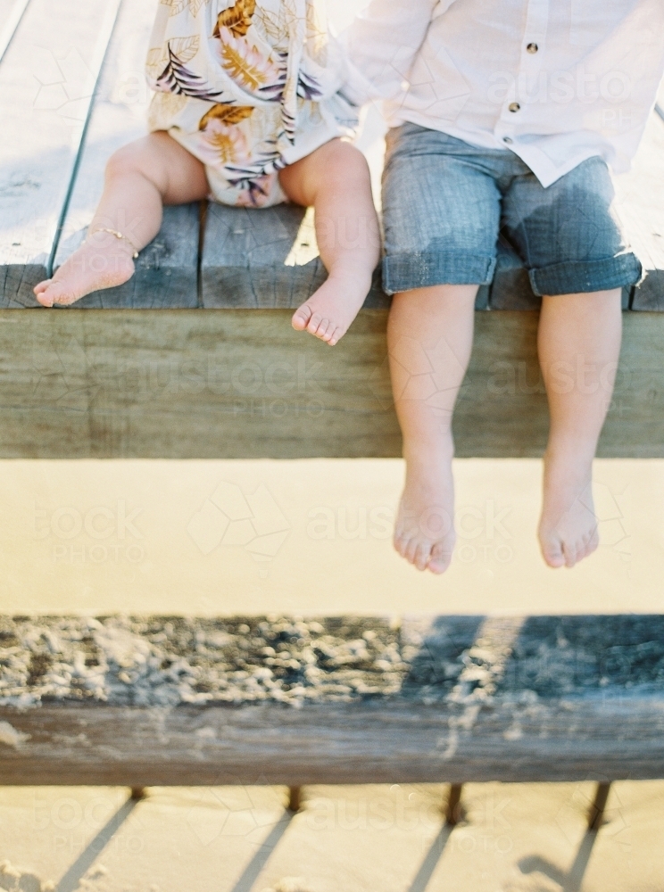 The legs of a young boy and baby hanging of the edge of a wharf - Australian Stock Image