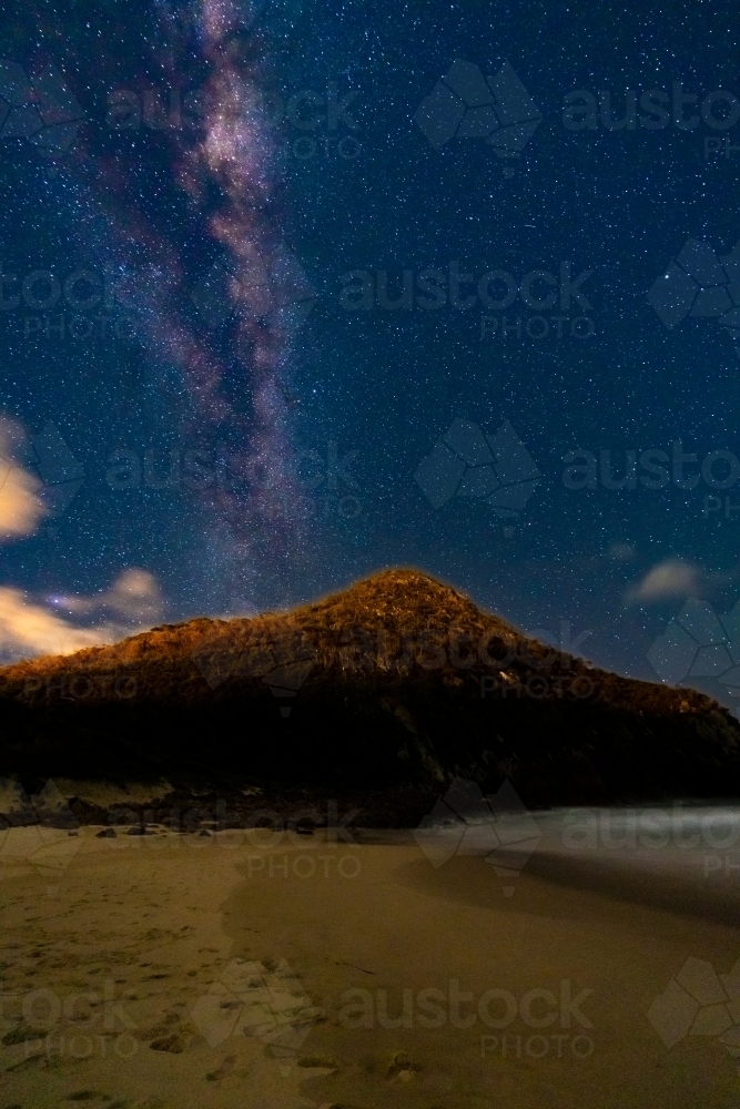 The Milky Way galaxy in the night sky over a beach and coastal mountain - Australian Stock Image