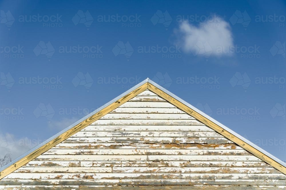 The peak of a tin roof and weatherboard house against a blue sky - Australian Stock Image
