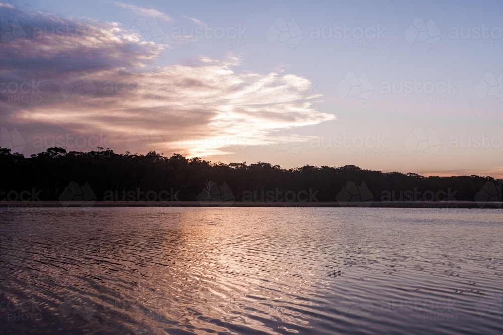 The setting dusk sun reflects on the ripples of a flowing lake. - Australian Stock Image