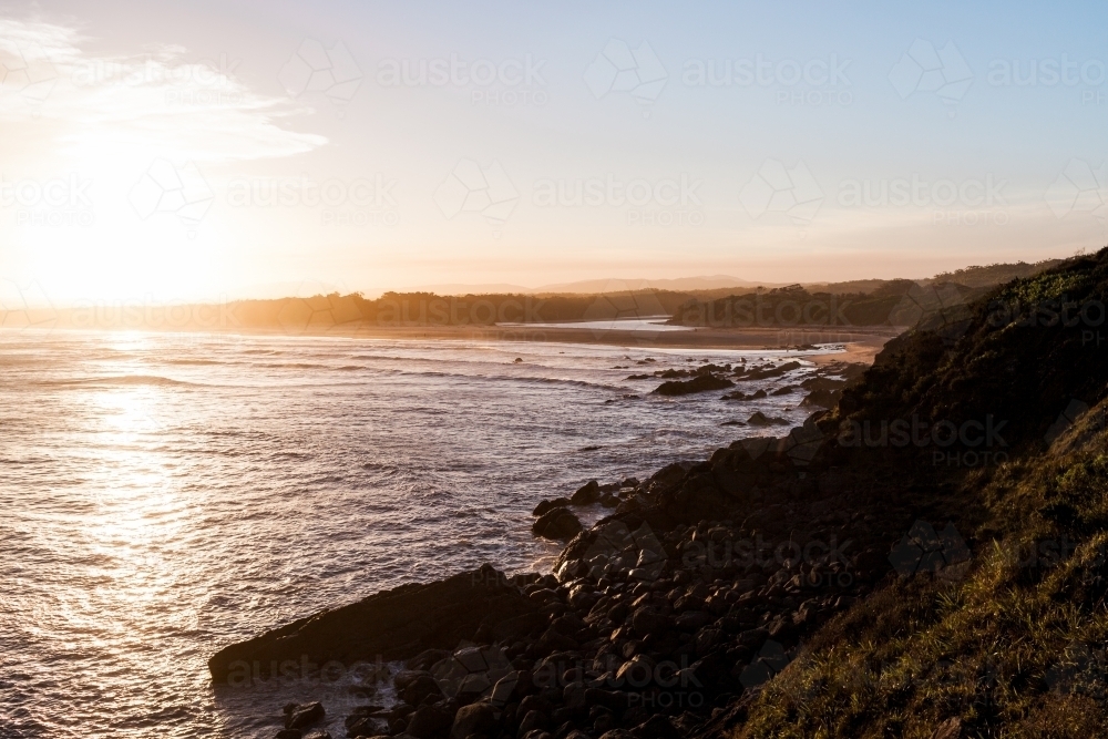 The setting sun reflects against the large ocean that is surround by nearby land and rocks. - Australian Stock Image