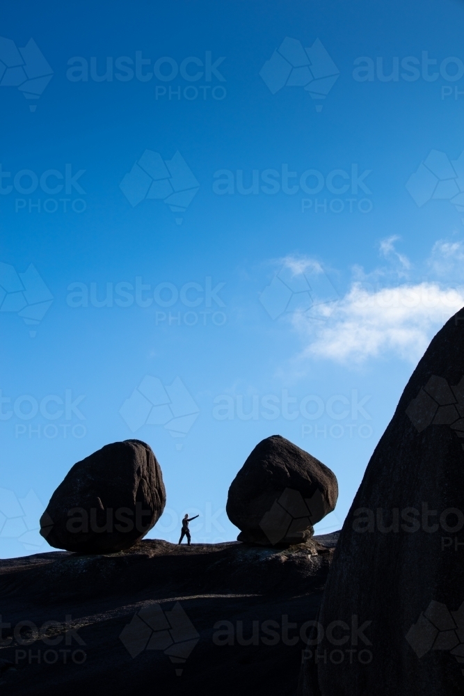 The small figure of a hiker pointing arm stands between two large round shaped boulders. - Australian Stock Image