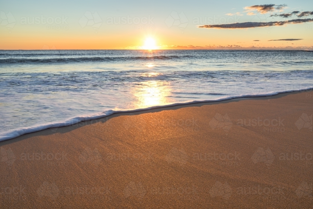 The sun rises over Collaroy Beach reflecting on water and sand - Australian Stock Image