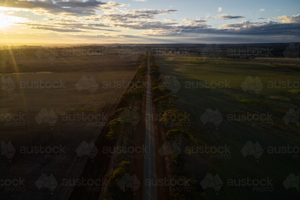 The sun rising over a farming landscape, with a bitumen road cutting through farmland in rural WA. - Australian Stock Image