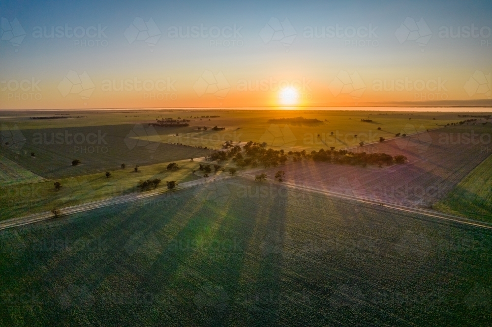 The sun rising over the horizon looking down on paddocks and trees streaming sun rays. - Australian Stock Image