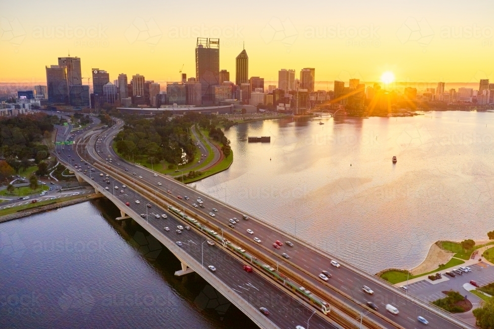 The sun rising over the Perth City skyline with the Narrows Bridge in the foreground. - Australian Stock Image