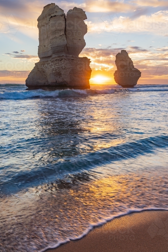 The Sun setting between two large sea stacks rising out out of the waves - Australian Stock Image
