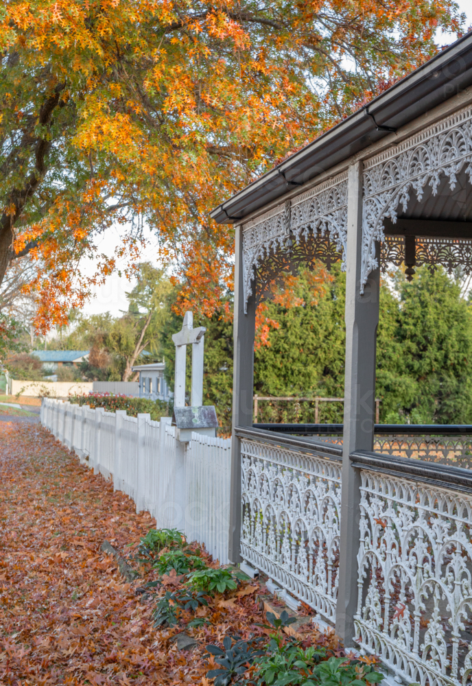 The wrought iron verandah of an old country home underneath orange leaves - Australian Stock Image