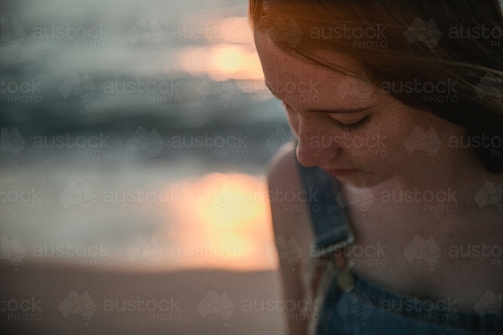 Thoughtful teenage girl on the beach at sunset wearing overalls - Australian Stock Image