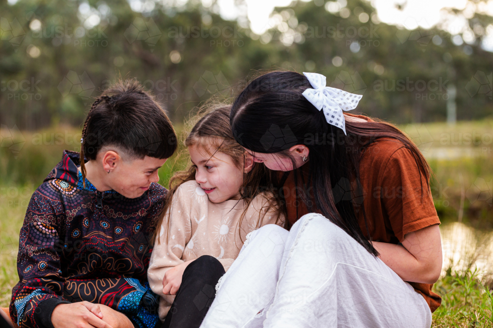 Three aboriginal kids hugging and smiling together outside - Australian Stock Image