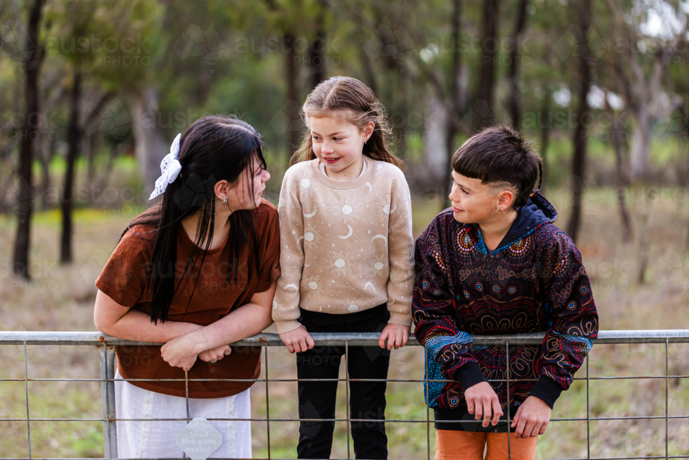 Three aboriginal kids leaning on fence together in paddock in winter - Australian Stock Image