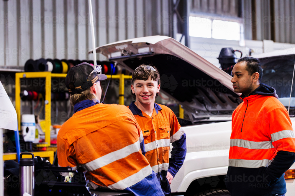 Three Australian men in industrial mechanics shed workplace chatting in conversation together - Australian Stock Image