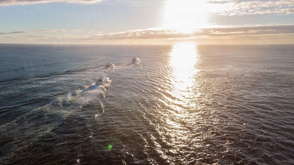 Three boats motoring towards sunrise off Gold Coast beach - Australian Stock Image