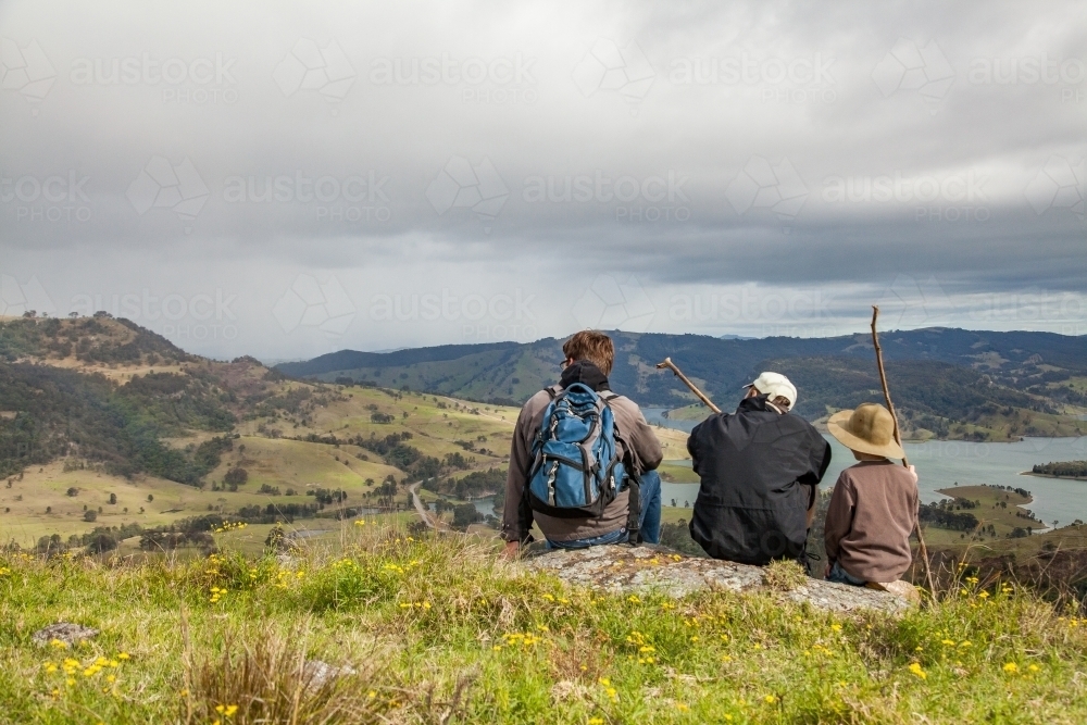 Three boys sitting on a rock in the hills watching rain come in - Australian Stock Image