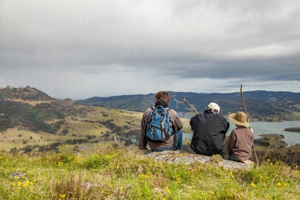 Three boys sitting on a rock in the hills watching rain come in - Australian Stock Image
