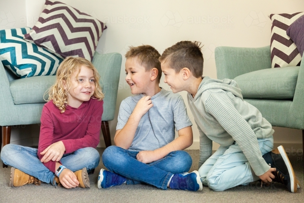 Three boys whispering and laughing with one another on floor - Australian Stock Image
