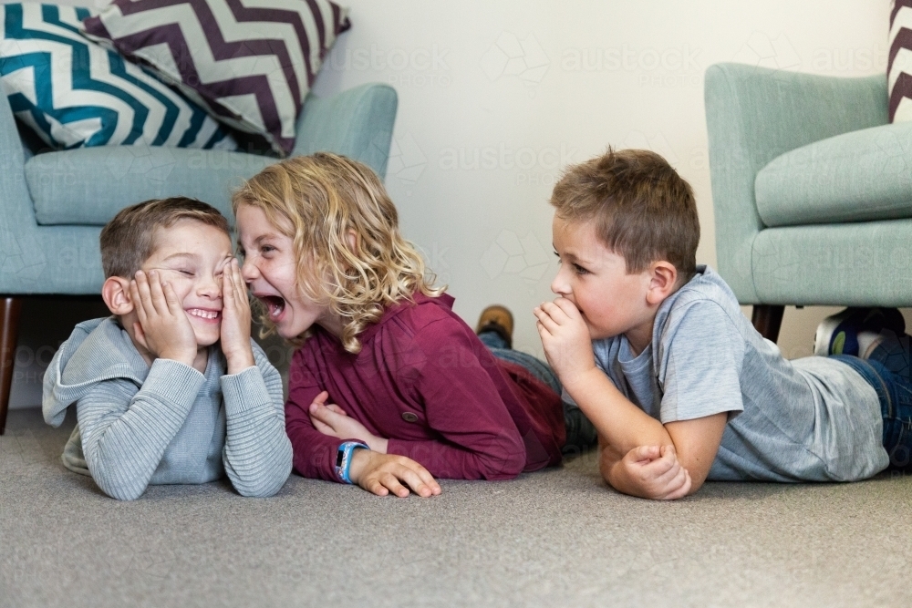 Three boys whispering and laughing with one another on floor - Australian Stock Image