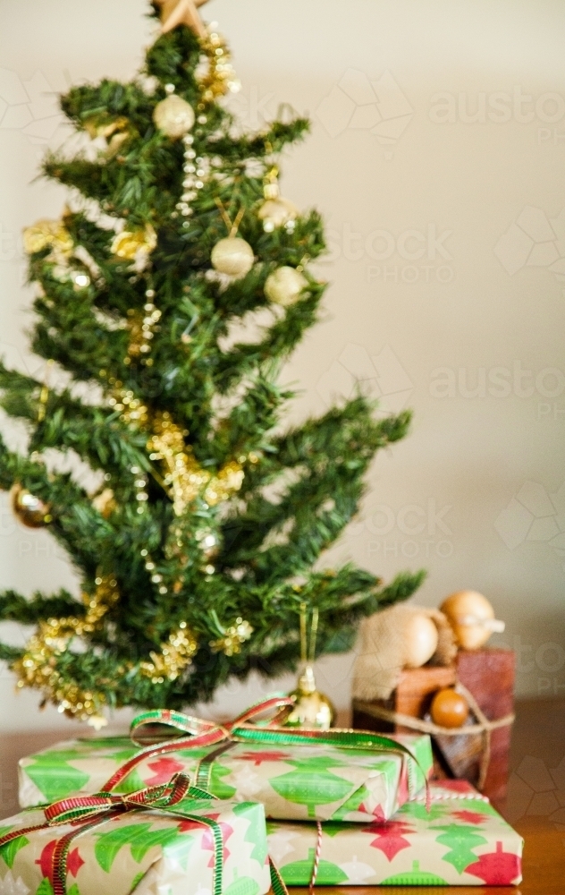 Three brightly wrapped Christmas gifts under a small decorated tree - Australian Stock Image