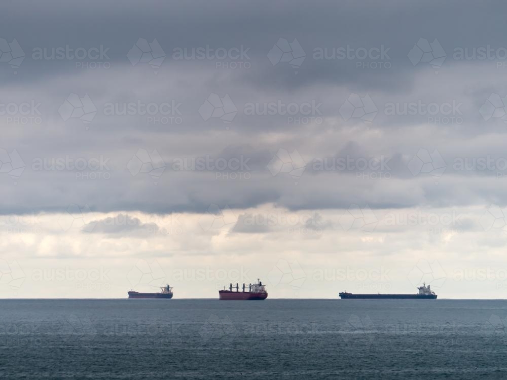 Three bulk carriers on the horizon on a cloudy day - Australian Stock Image