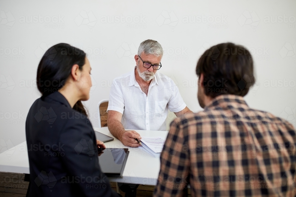 Three business people sitting at a desk, talking in a studio - Australian Stock Image