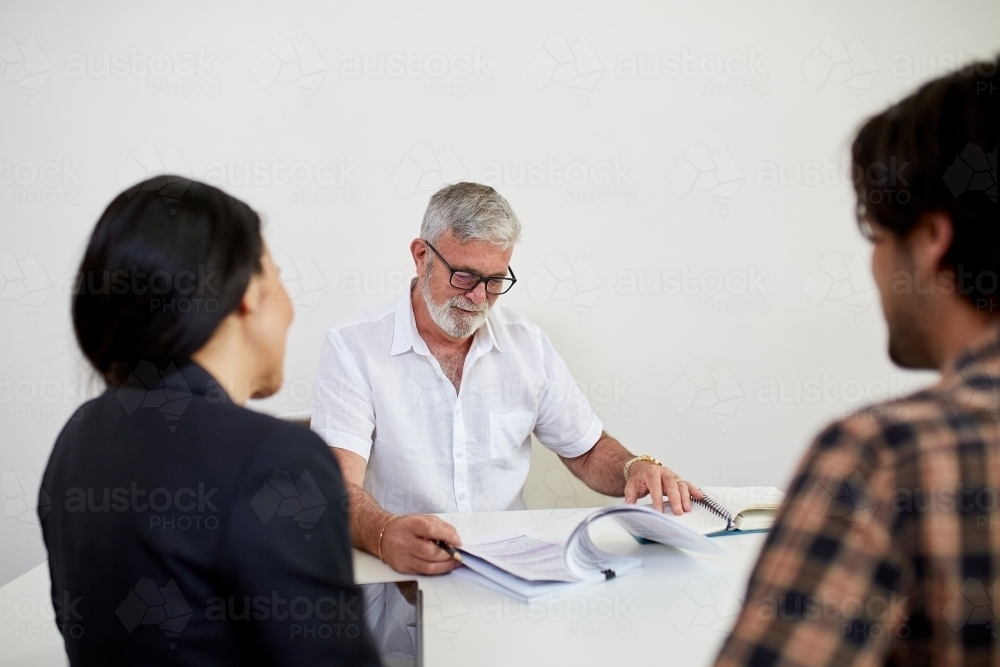 Three business people sitting at a desk, talking in a studio - Australian Stock Image