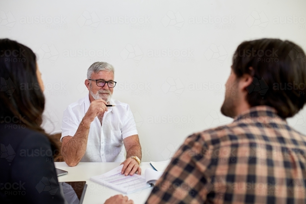 Three business people sitting at a desk, talking in a studio - Australian Stock Image