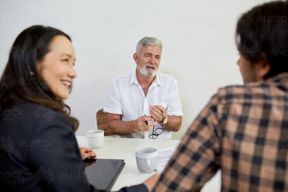 Three business people sitting at a desk, talking in a studio - Australian Stock Image