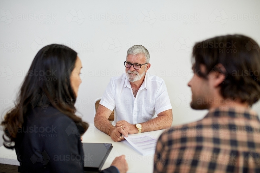 Three business people sitting at a desk, talking in a studio - Australian Stock Image