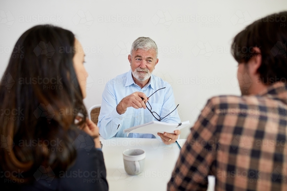 Three business people sitting at a desk, talking in a studio - Australian Stock Image