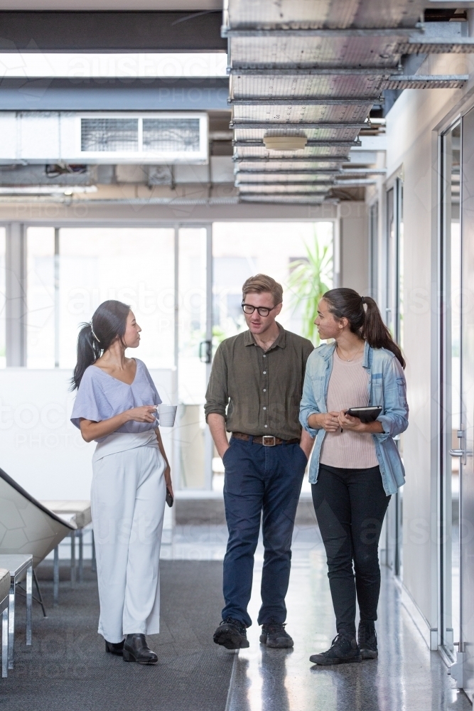 Three businesspeople walking through office hall and talking - Australian Stock Image