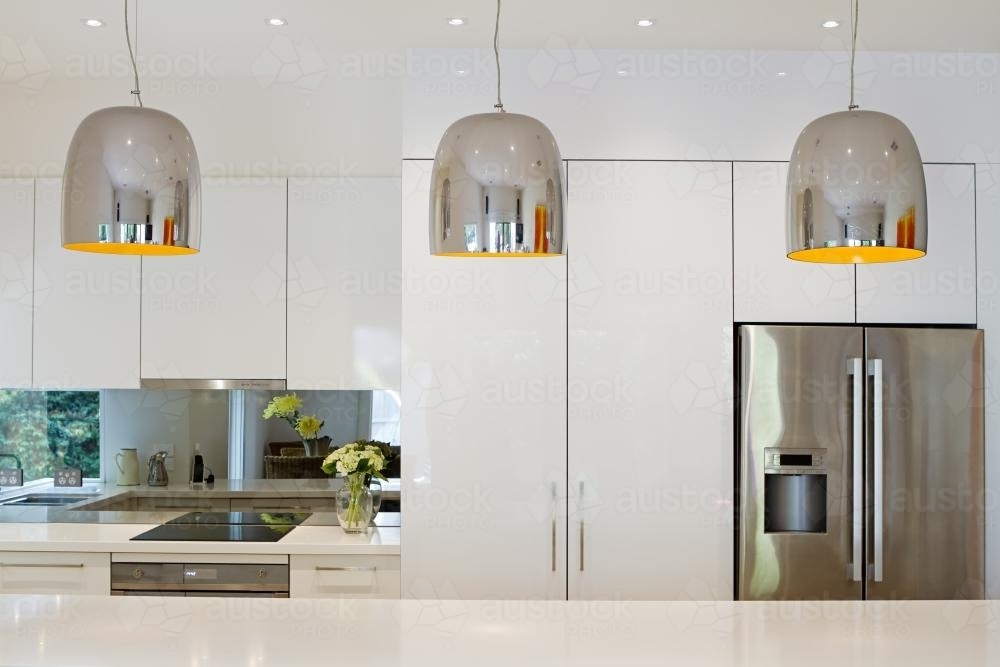 Three chrome pendant lights hanging over kitchen island bench - Australian Stock Image