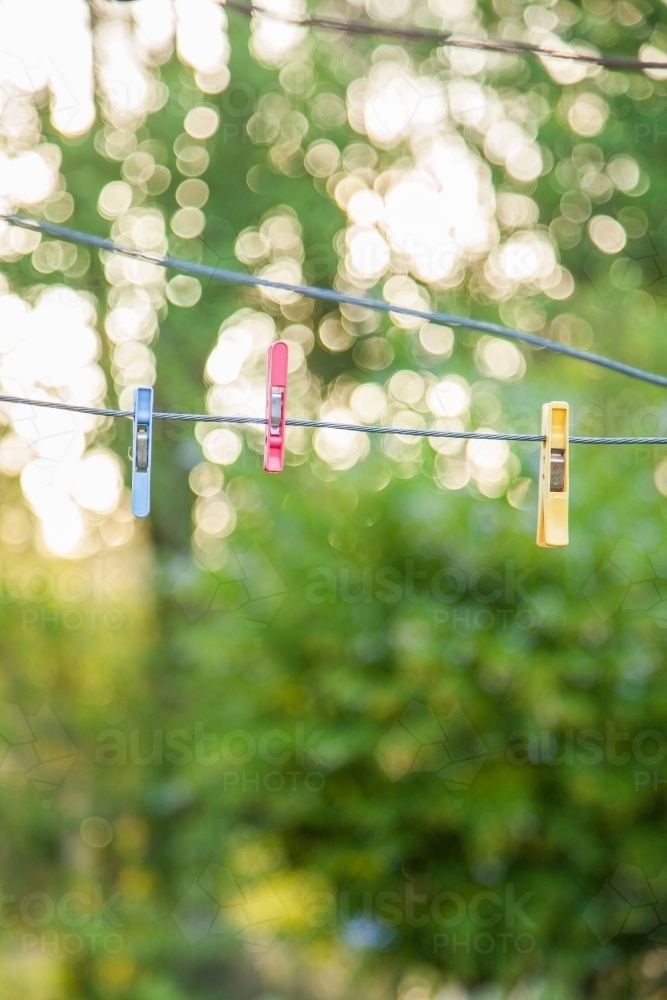 Three coloured clothes pegs hanging on an empty line with bokeh background - Australian Stock Image