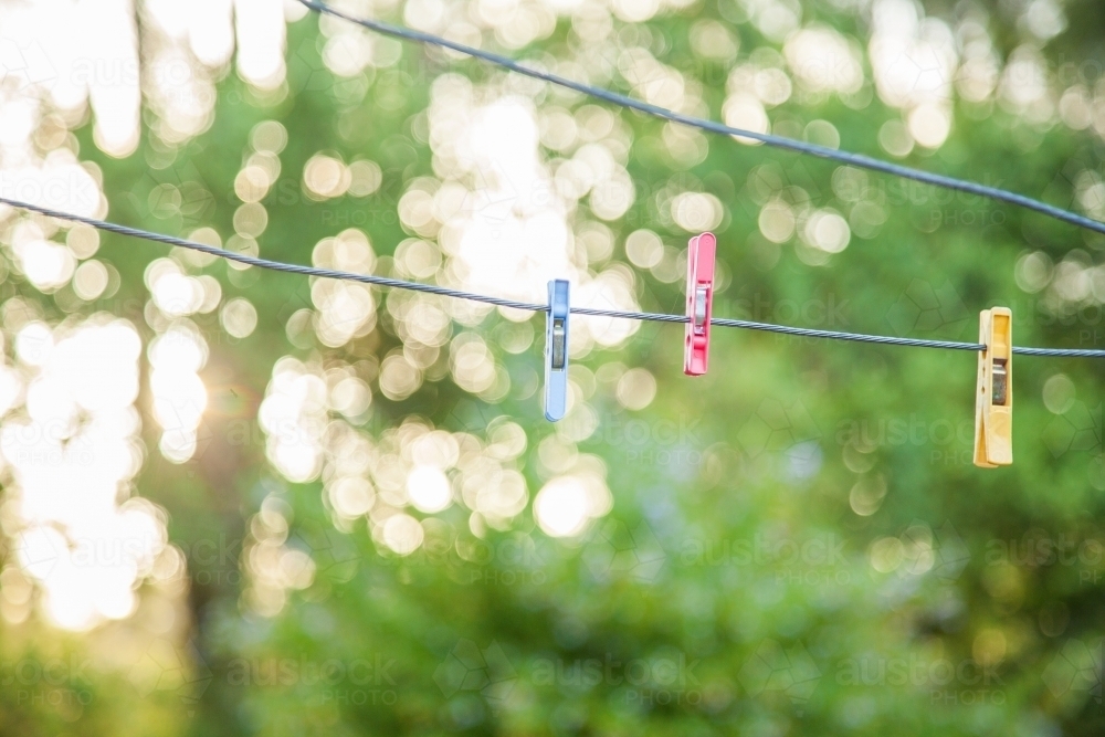 Three coloured clothes pegs hanging on an empty washingline with bokeh background - Australian Stock Image