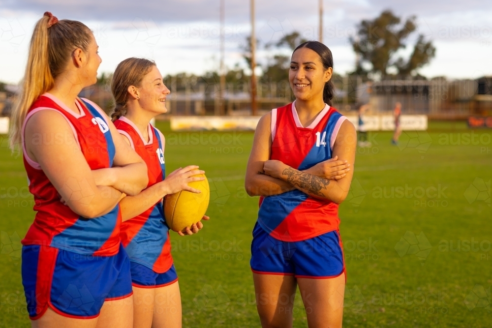 three female Australian footballers standing on oval with one holding football - Australian Stock Image
