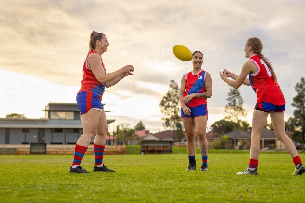 three female footballers practising ball handling skills at sunset - Australian Stock Image