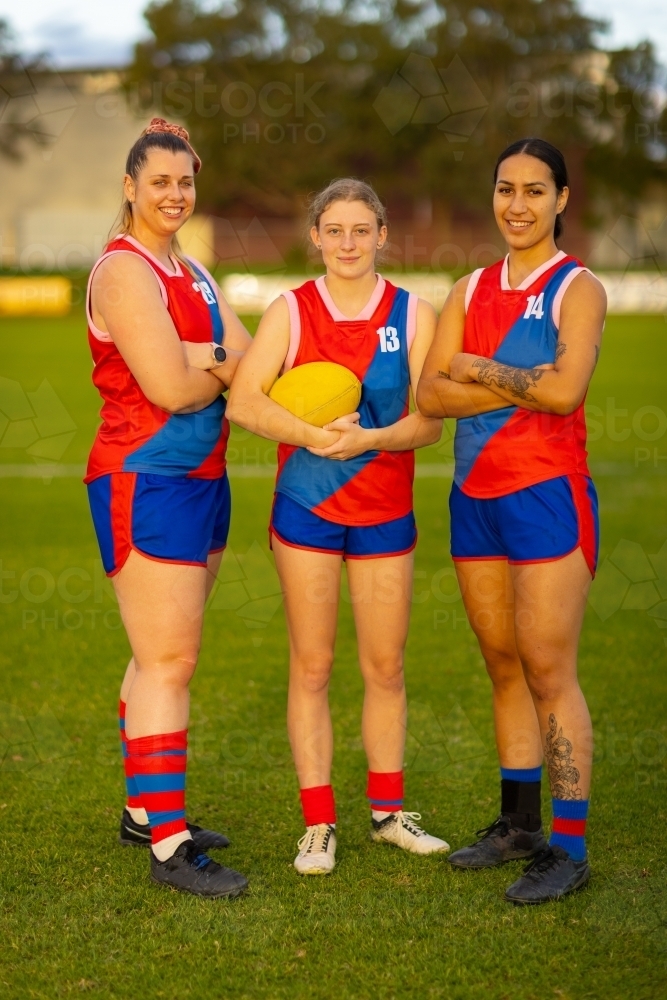 three female footballers standing on oval with arms crossed - Australian Stock Image