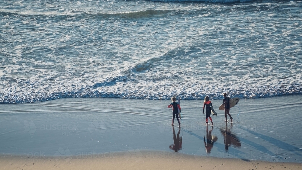 Three female surfers entering the ocean : Austockphoto Three female surfers entering the ocean - Australian Stock Image