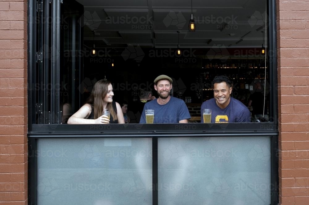Image of Three friends at a window having a drink at a local craft beer ...