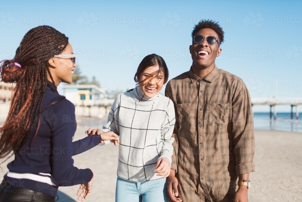 Three friends laughing together on the beach - Australian Stock Image