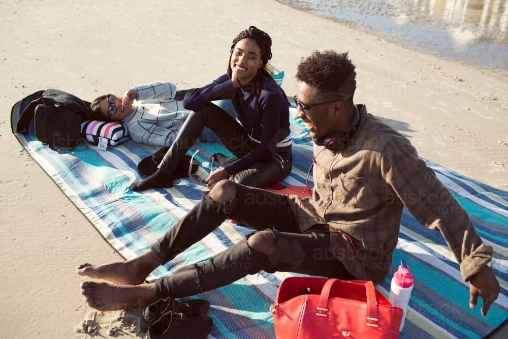 Three friends on a picnic blanket relaxing at the beach - Australian Stock Image