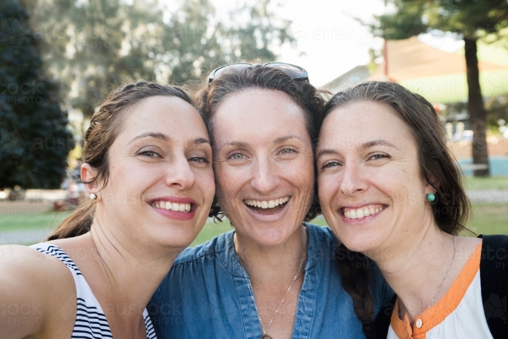 Three friends taking a selfie while smiling at the camera in a park. - Australian Stock Image