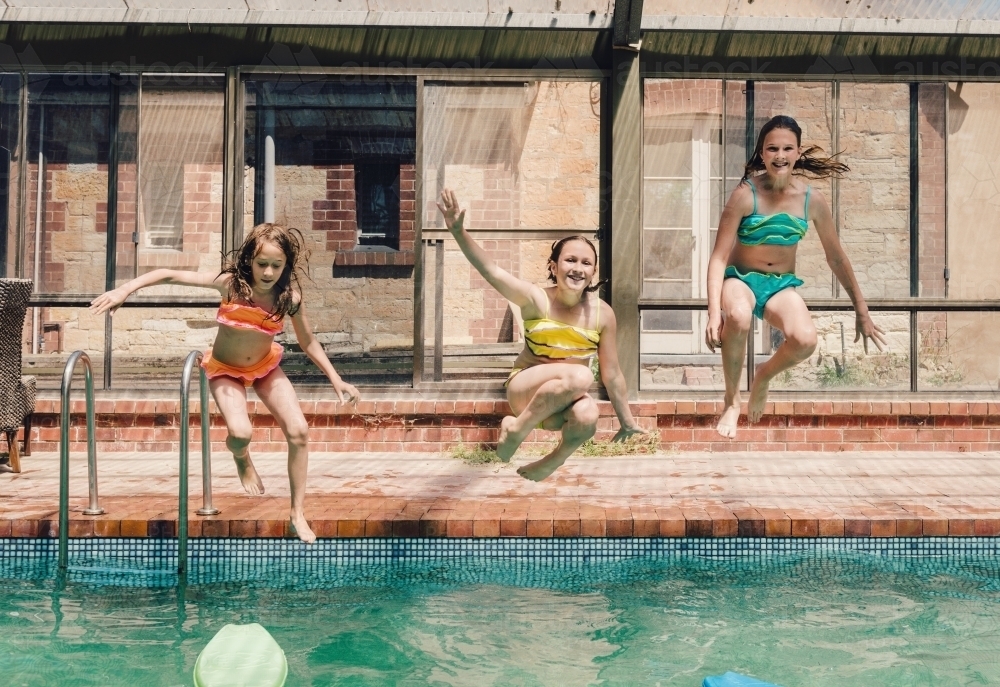 Three girls jumping into a swimming pool - Australian Stock Image