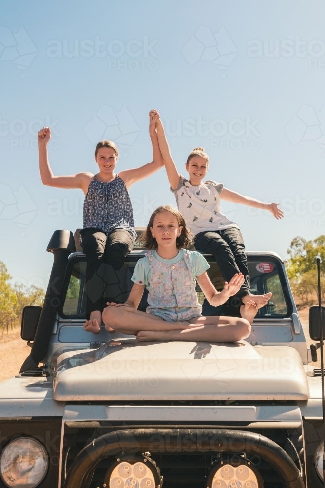 Three girls sitting on the hood of a four wheel drive in outback australia - Australian Stock Image