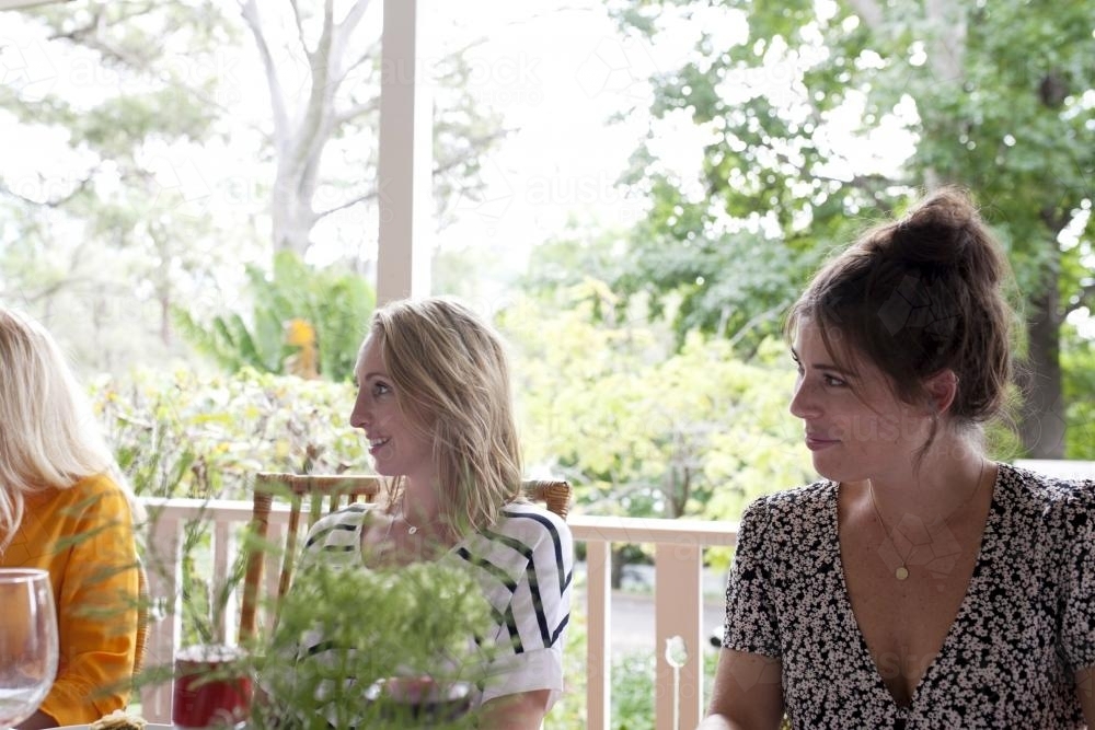 Three girls smiling whilst sitting on verandah - Australian Stock Image
