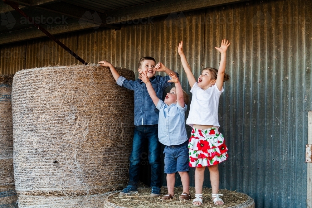 Three happy children on hay bales at farm - Australian Stock Image